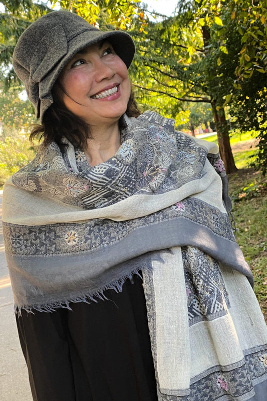 Smiling woman wearing a grey bucket hat with grey and creme scarf.
