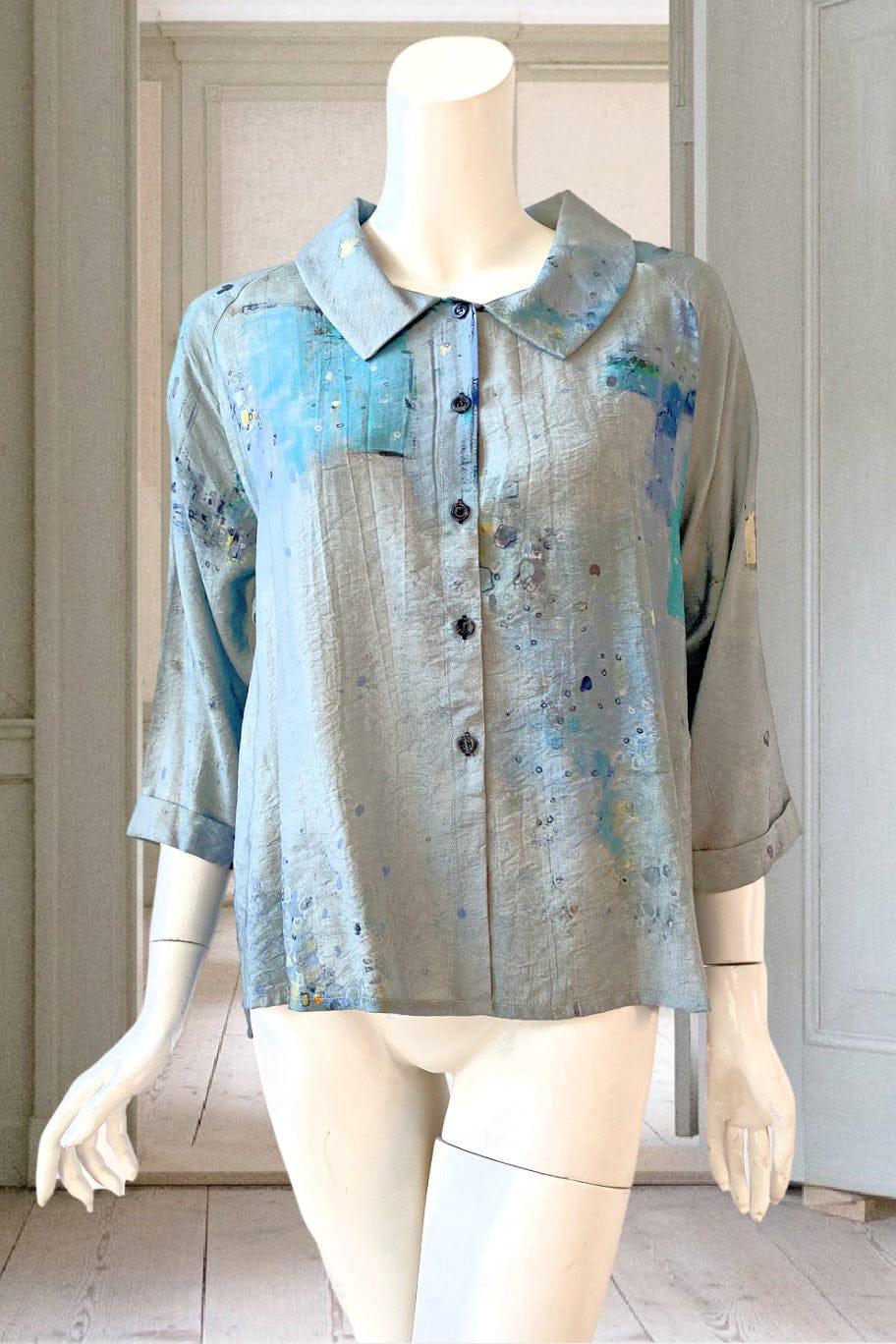 Pretty women's crop button down with 3/4 length sleeves. Blue tones with an artistic scatter print. The blouse is worn by a manequin..