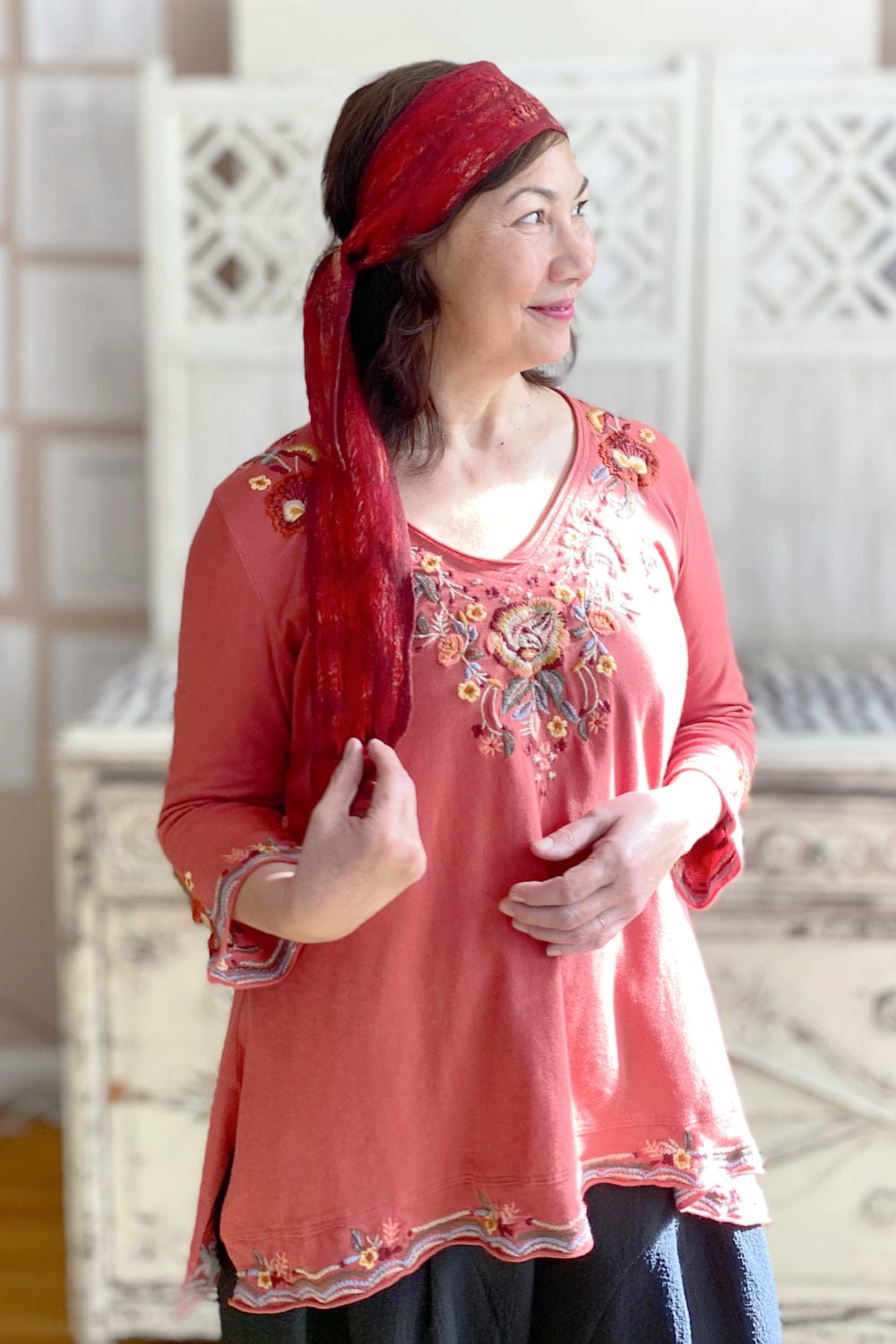 Woman with red head scarf wearing a jersey knit v neck top with embroidery detail.