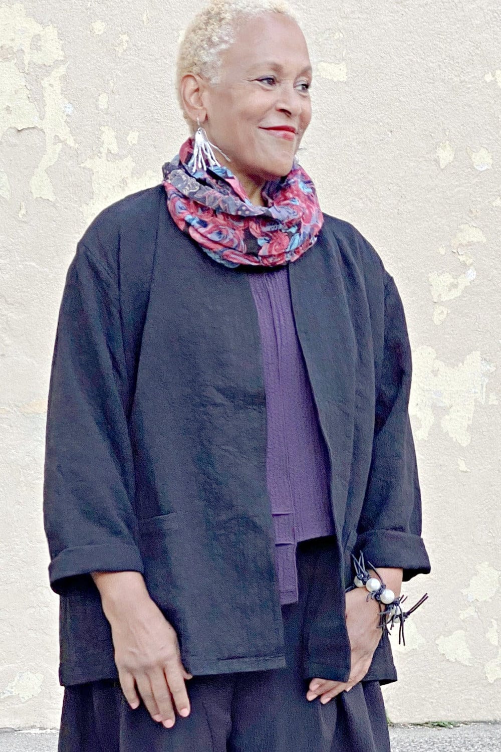 Textured heavy cotton boxy jacket worn over a plum uneven hem top. The older model is also styled with a floral scarf, silver spikey earrings and a black leather spike brackelet.
