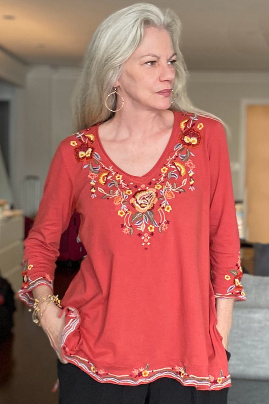 Older woman with long grey hair wearing a styling outfit of an embellished top, hoop earrings and wired stacked bracelet.