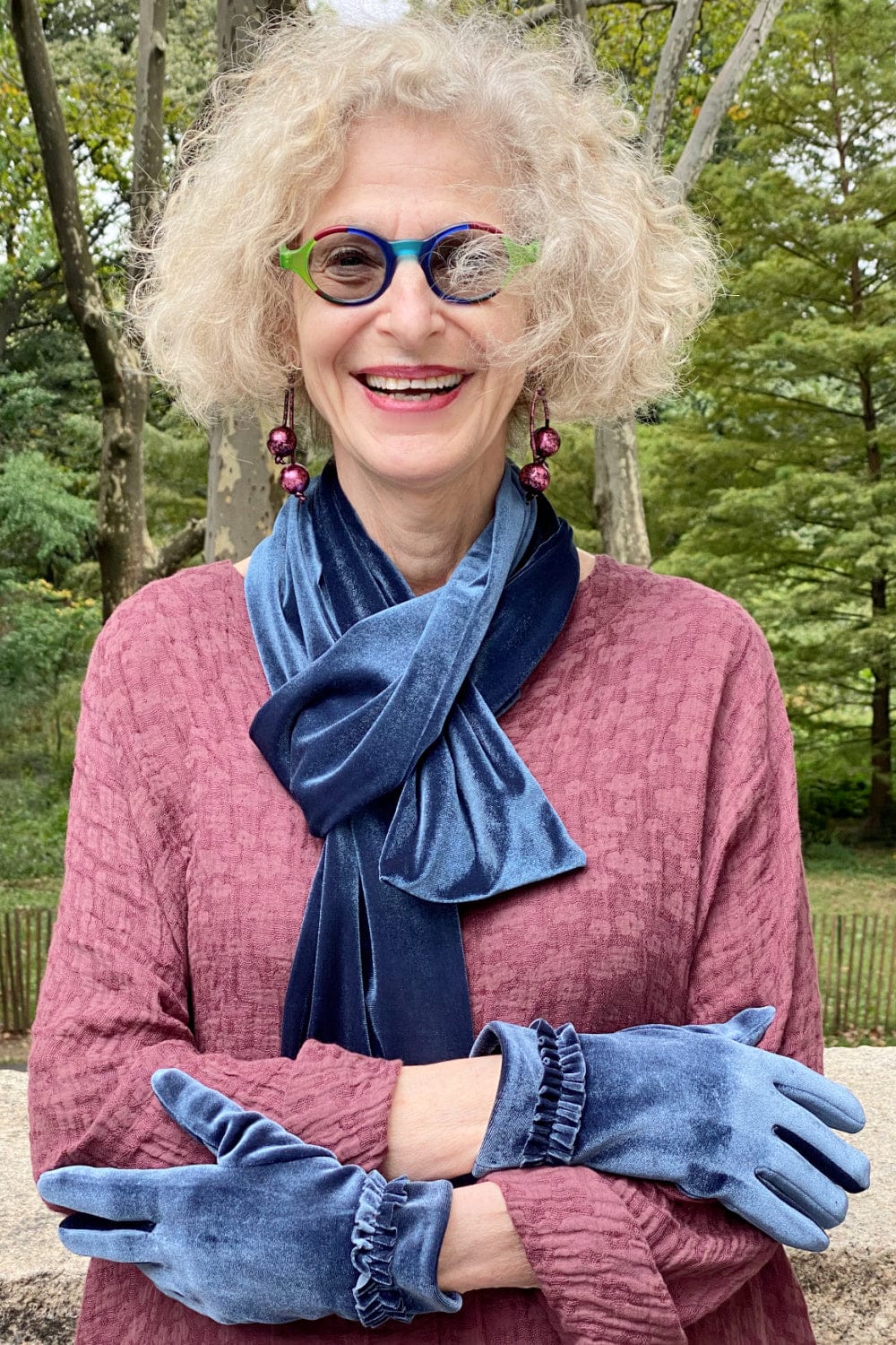 Smiling woman wearing a vintage blue velvet scarf and matching gloves with a rose jacket.
