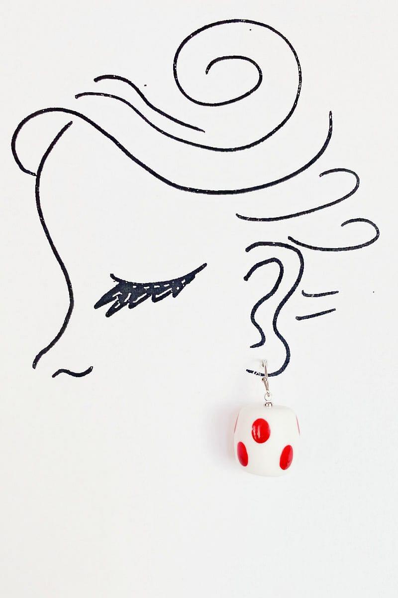 Round shaped white earrings with handpainted red dots .