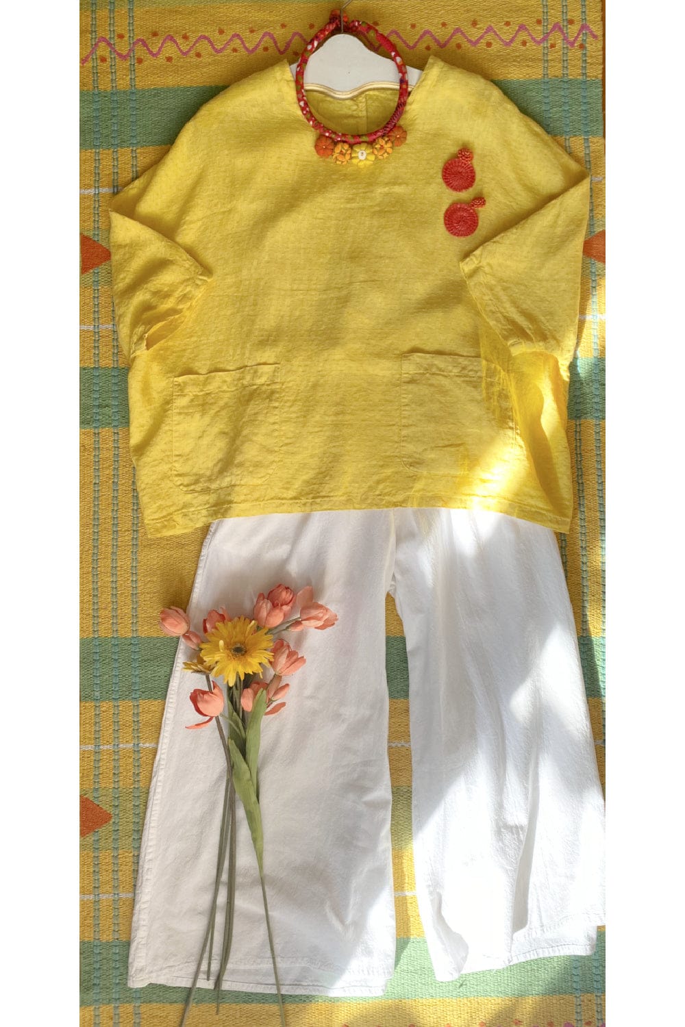 Pretty textile necklace is soft reds and yellows styled with a yellow boxy linen top and full cut white cotton pants.
