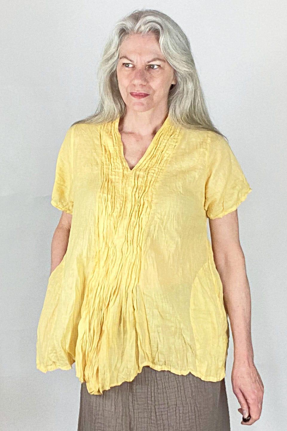 Older woman with long grey hair wearing a front gathered yellow cotton blouse with short sleeves